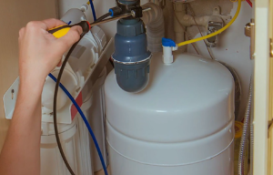 A close-up image of a water leak detector placed under a kitchen sink, with visible water droplets nearby.